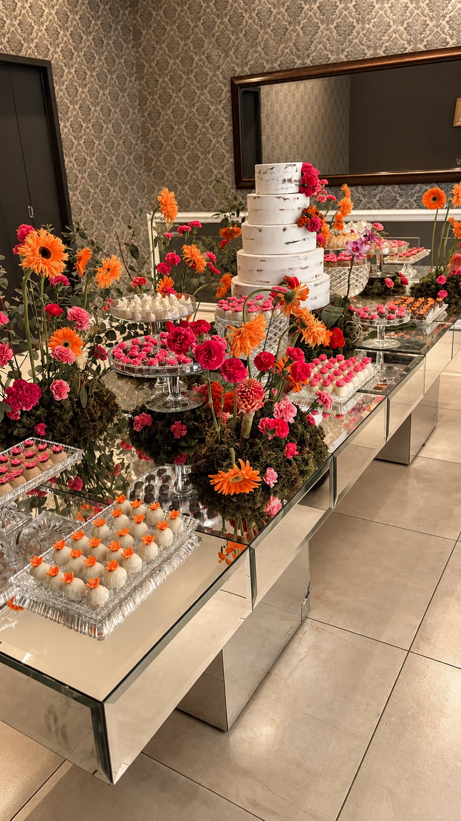 Mesa de doces com tampo espelhado, flores coloridas e doces variados