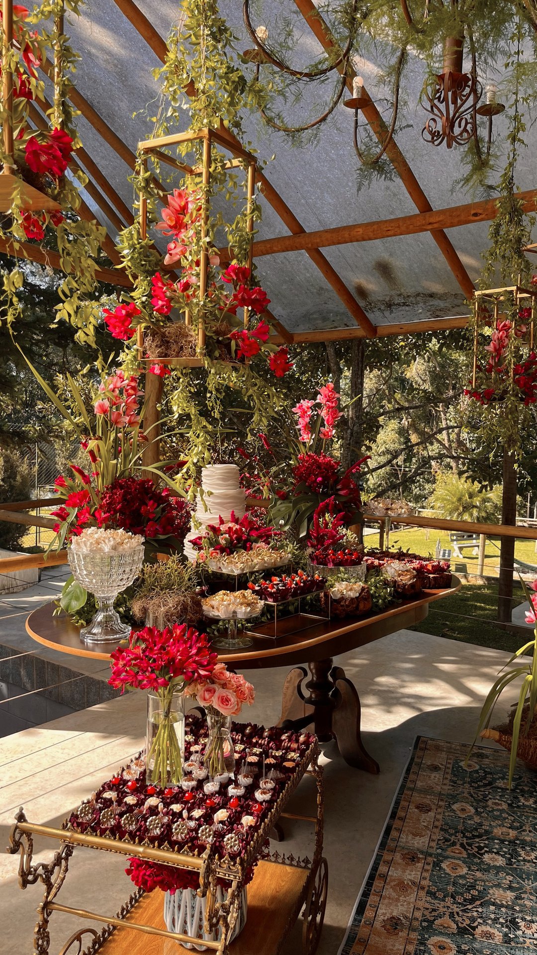Mesa de doces com flores vermelhas e bolo, sob estufa de vidro